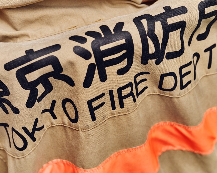 Wet firefighters' protective coats with Japanese characters printed in black hang over beige chairs to dry after drills.