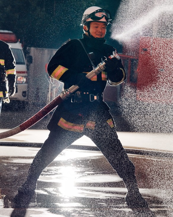 Tokyo firefighter in protective gear spraying water from hose during training exercise.