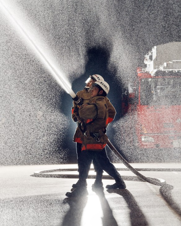 Firefighter in protective gear spraying water from a hose during training exercise