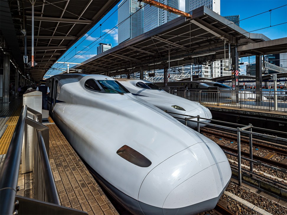 White Tokaido Shinkansen bullet trains at platform under covered station canopy with city skyline beyond.