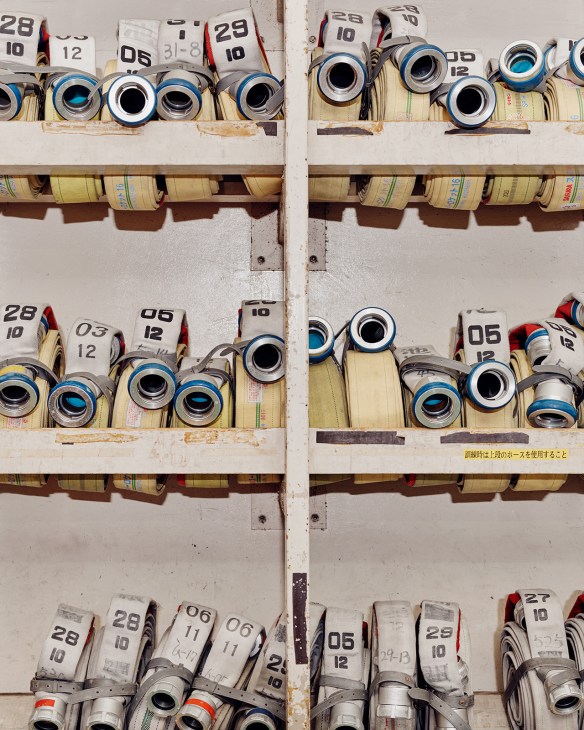 Neatly organized fire hoses rolled and stored on shelves with numbered labels at Ikebukuro Fire Station.