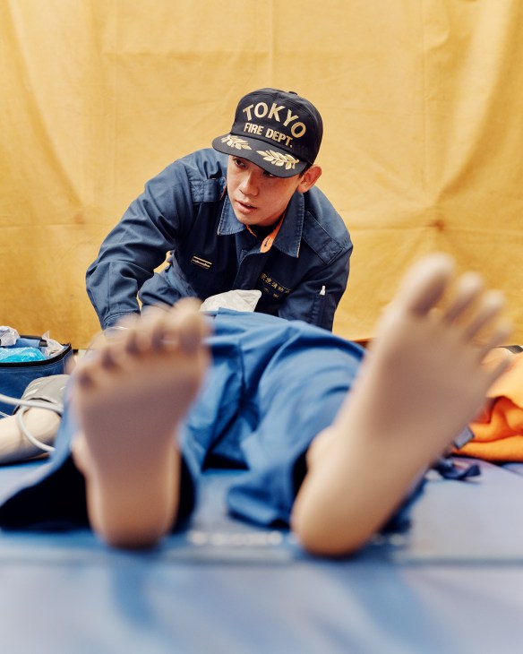 Tokyo Fire Department paramedic in uniform training on a medical dummy during basement drill.