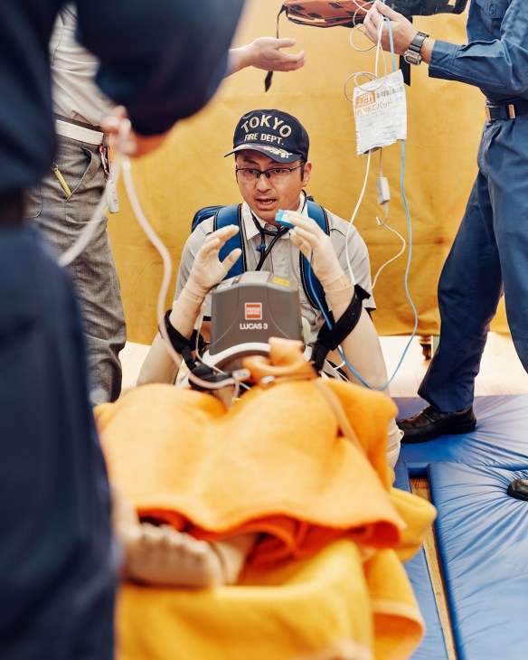 Tokyo Fire Department trainer demonstrating rescue equipment to surrounding firefighters during training exercise.