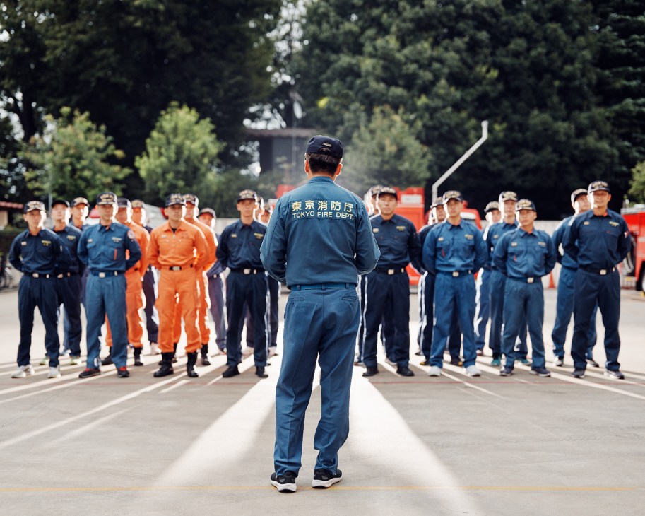 Tokyo Fire Department commander addresses firefighters in blue uniforms gathered during training session
