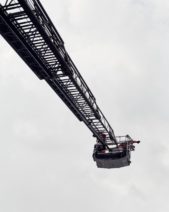 Firefighter on extended ladder demonstrating hand signals during Tokyo Fire Department training drill.