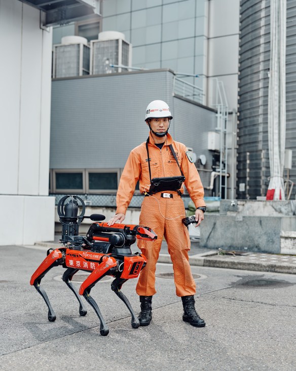Tokyo firefighter Ryo Yokota stands with the Tokyo Fire Department's four-legged rescue robot in urban setting.