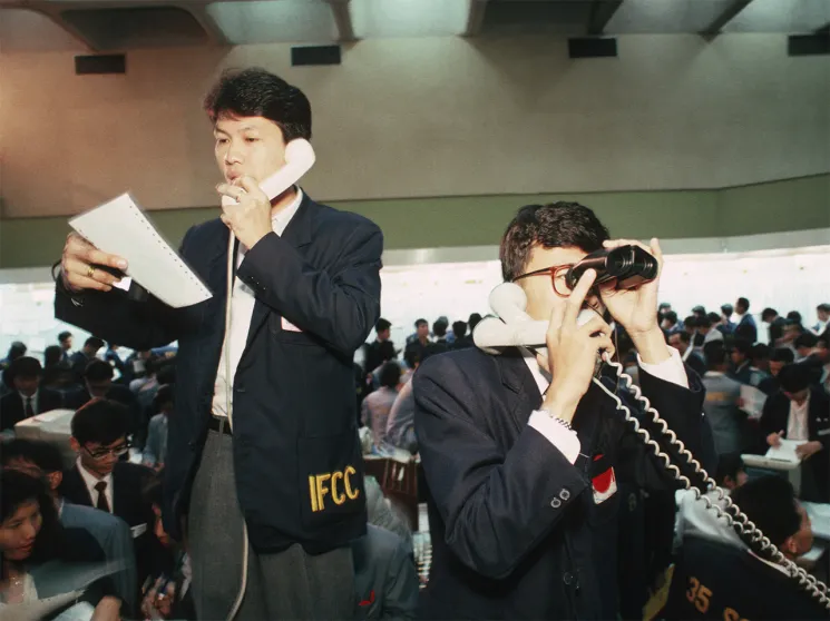 The Thai Stock Exchange in 1989 prior to becoming computerized. Brokers take orders on their headphone sets and use binoculars to see the stock boards where share prices are displayed.