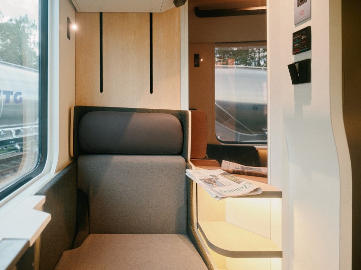 Interior of Nox's refitted sleeper train carriage featuring a gray upholstered seat with wooden paneling and warm lighting.