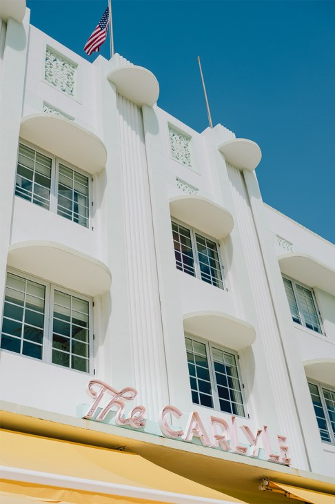 The Tiffany hotel building in South Beach with white art deco facade, curved balconies, and pink neon signage.