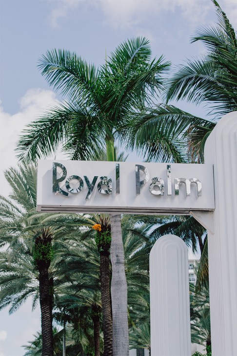 Royal Palm hotel sign with metallic lettering on white facade surrounded by palm trees.