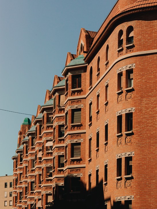 Red-brick facade of Finca Roja housing complex in Valencia with stepped gable roofs and regular window patterns.