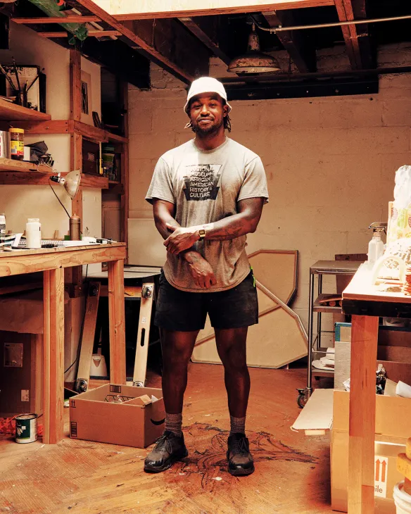 Woodworker Mike Haynes standing in his workshop wearing a white cap and gray t-shirt.
