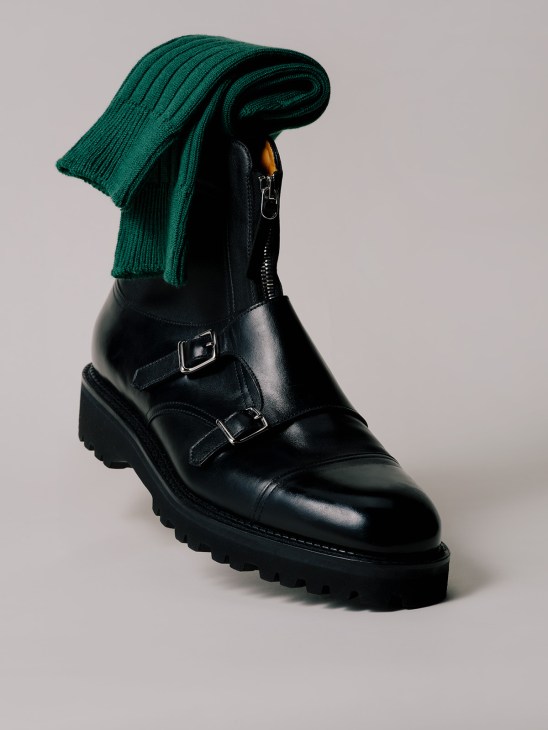 Black leather lace-up boots with buckle straps and chunky tread sole, styled with green knit socks.