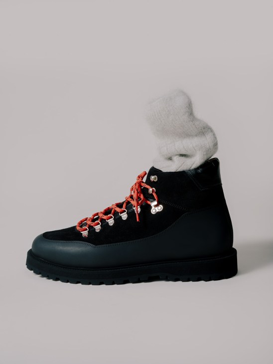 Black hiking boot with red laces and white cuffed sock against gray background