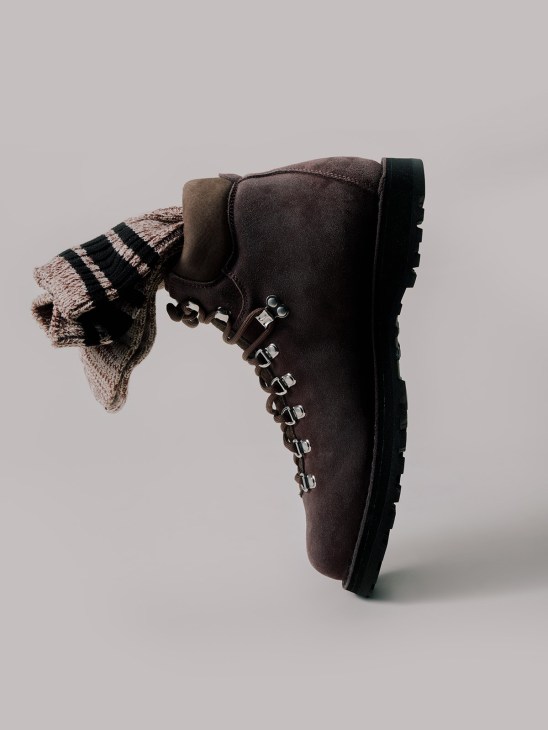 Dark brown suede lace-up boot with metal D-ring lacing details and knit wool socks with black striping.