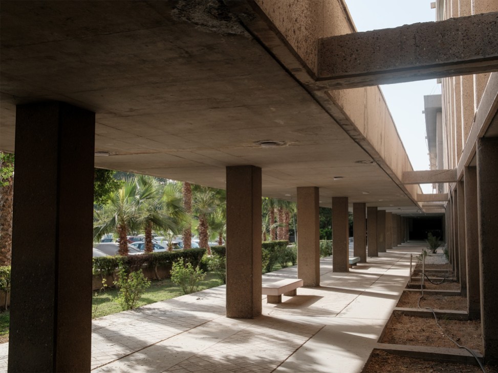 Covered walkway with concrete columns at Walter Gropius-designed University of Baghdad campus with palm trees visible beyond