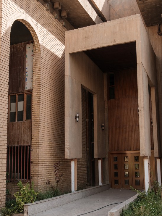 Entrance to a brutalist building by Rifat Chadirji featuring brick and concrete with arched doorway and wooden doors.