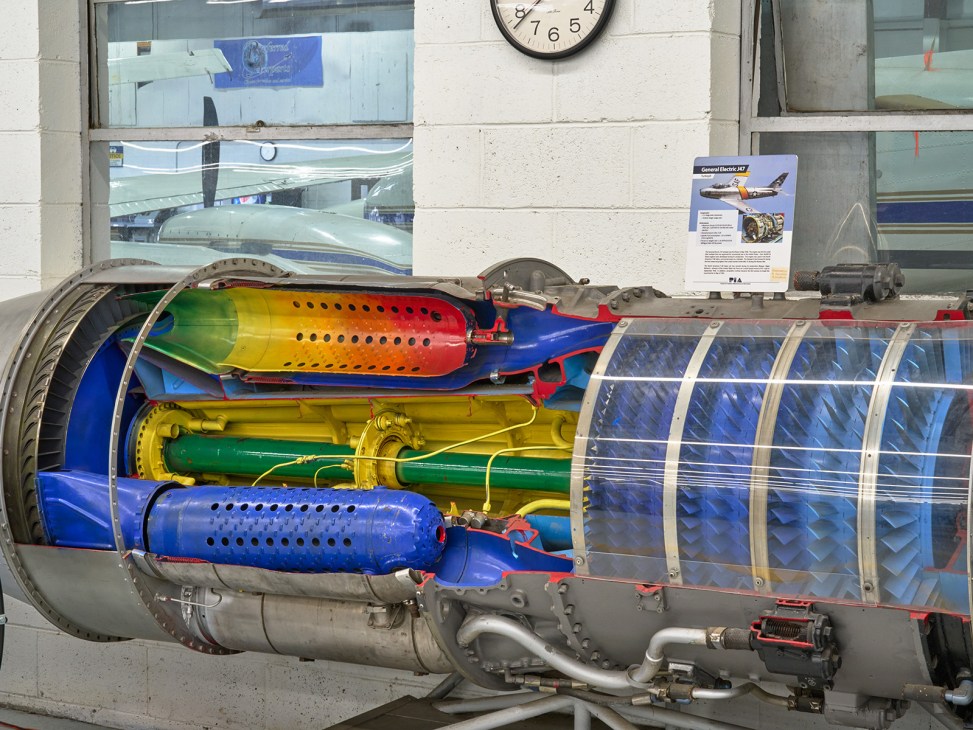 Cutaway display model of an aircraft turbofan engine showing colorful internal components including compressor stages, combustion chamber, and turbine sections.