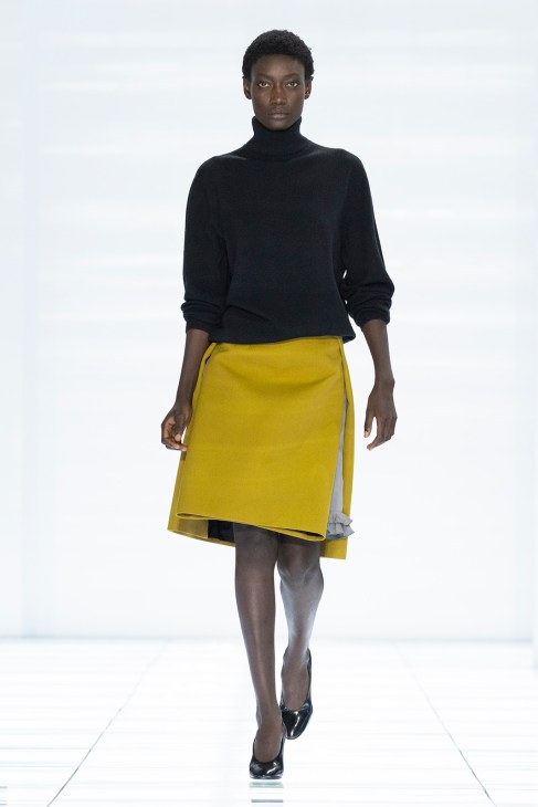 Model wearing black turtleneck sweater and yellow skirt with gray underlay detail.