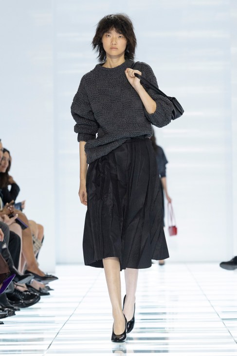 Model on runway wearing charcoal knit sweater and black pleated midi skirt from Prada spring/summer 2027 collection
