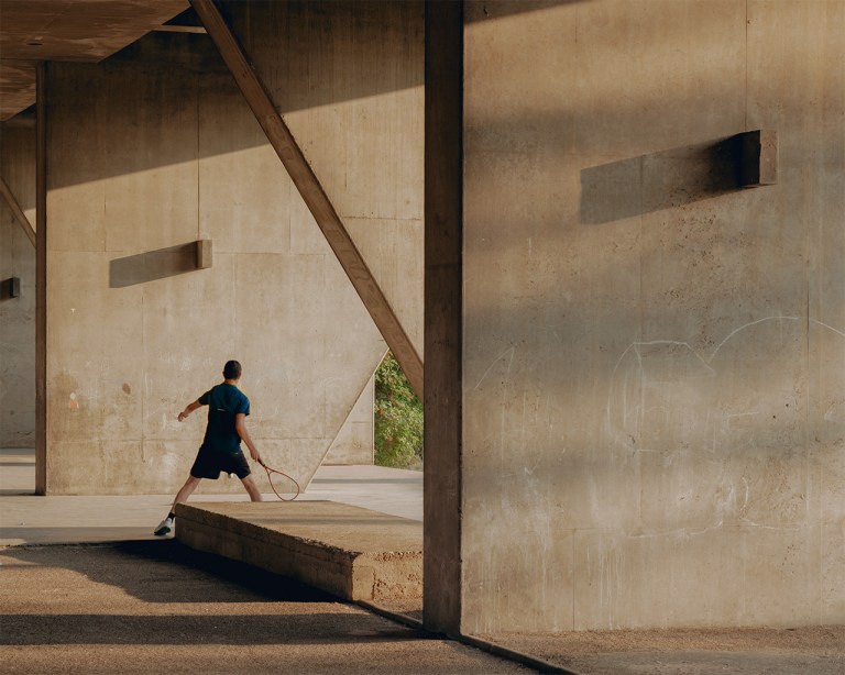 Person playing badminton under a concrete overpass in Saint-Étienne, France.