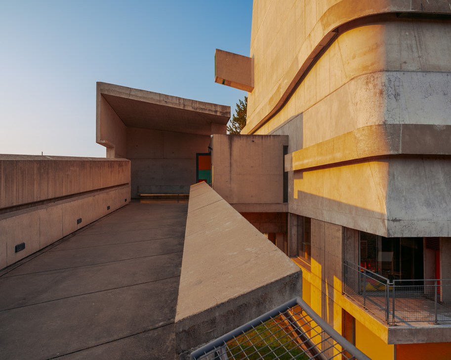 Exterior view of Église Saint-Pierre with brutalist concrete architecture and yellow-painted structural elements against clear sky.