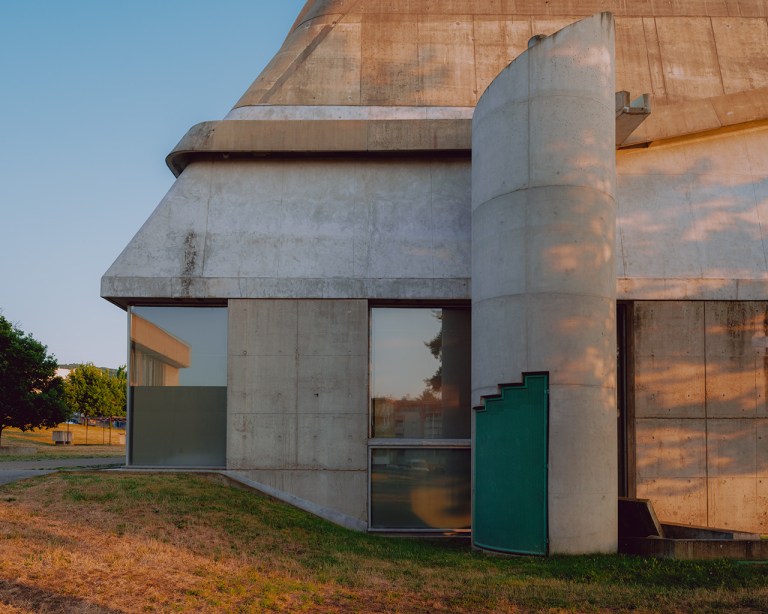 Concrete modernist building with cylindrical tower, large windows, and green door in Saint-Étienne.