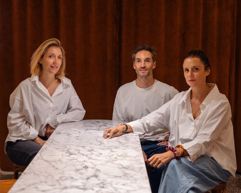 Three designers seated at a marble table against a brown curtain backdrop.