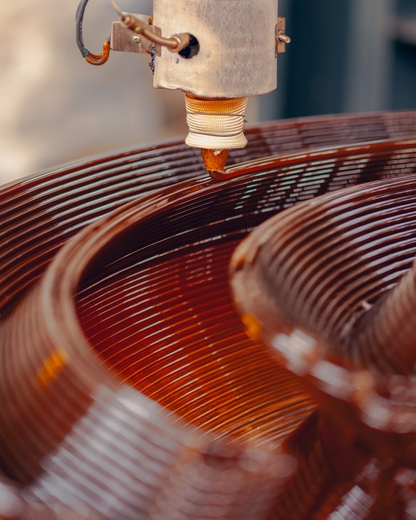 Close-up of a 3D printer nozzle depositing colorful recycled plastic layers onto a circular object
