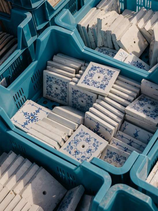 Overhead view of blue plastic crates filled with salvaged white ceramic tiles decorated with blue patterns, stacked in Rotor DC's warehouse.