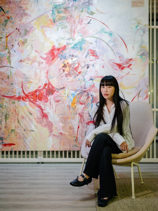 Woman seated in chair against abstract colorful painting with red, pink, and blue brushstrokes