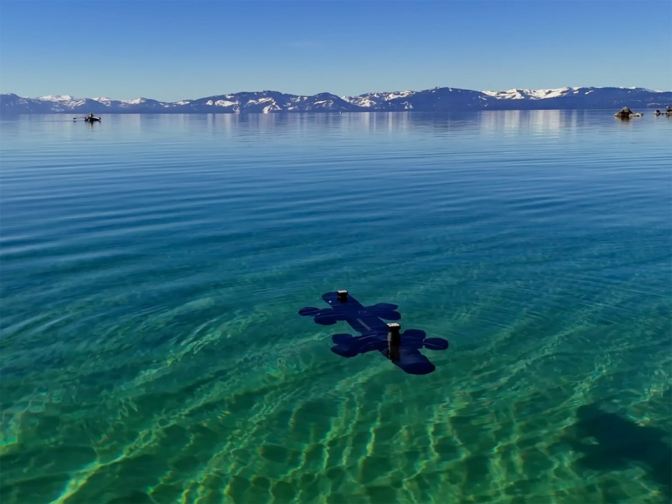 Ulysses autonomous marine drone underwater in clear blue water with snow-capped mountains visible across the bay
