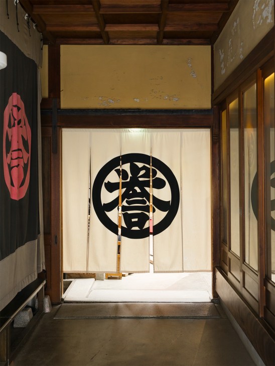 Interior entrance of Kondaya Genbei featuring a traditional noren curtain with black circular family crest design