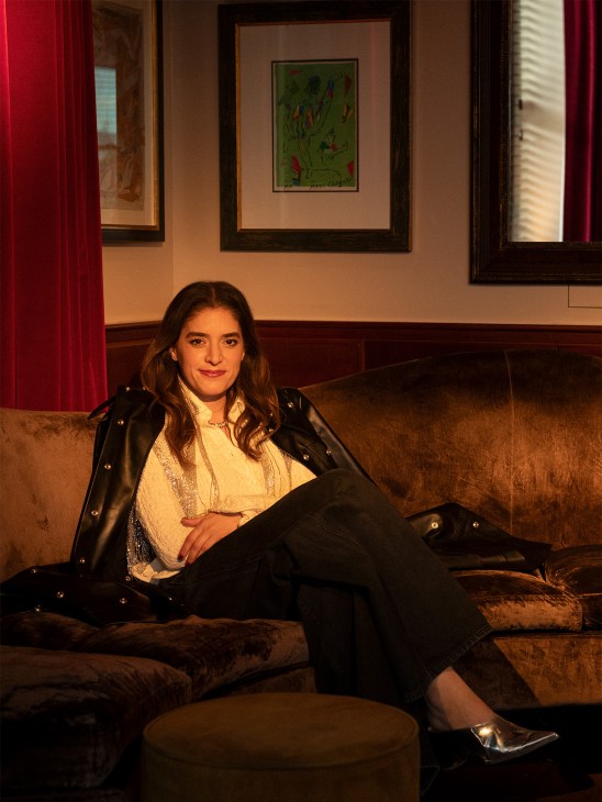 Stephanie Barba Mendoza seated on a brown velvet sofa against a warm-toned wall with framed artwork.