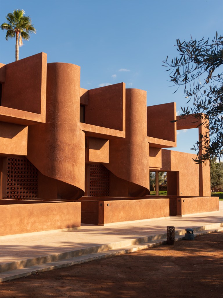 Villa El Fida's terracotta-colored modernist façade with geometric forms, featuring cylindrical towers and rectangular openings against a clear blue sky.