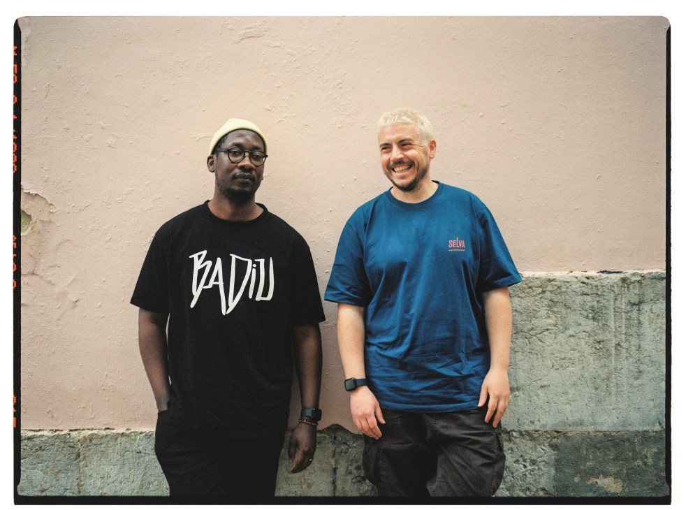 Epalanga and Branko standing together against a beige wall