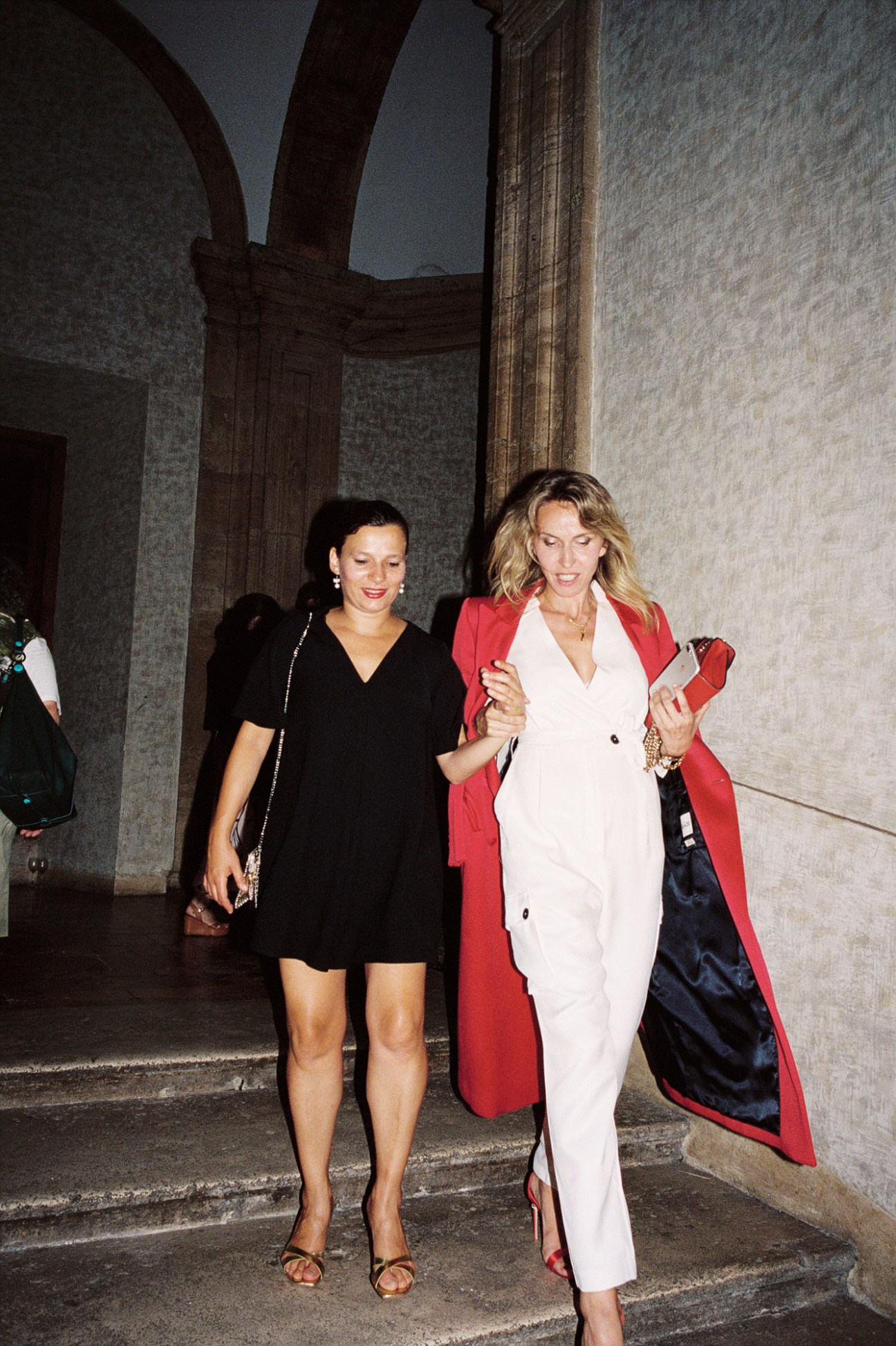 Two women in elegant evening wear walking down stone steps at night