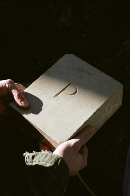 Hands holding a white stone block with carved letter P