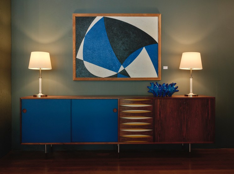 Mid-century modern wooden sideboard with blue cabinet doors and geometric abstract artwork above