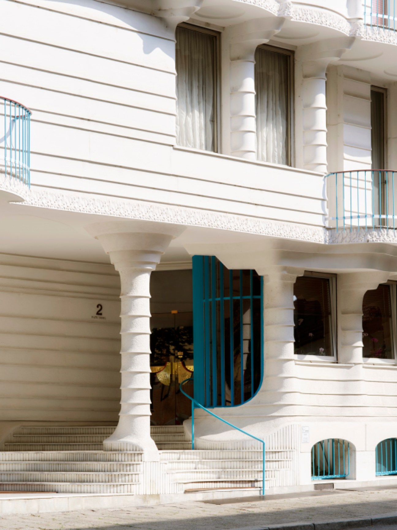 Casa dell'Obelisco white concrete facade with curved columns, turquoise railings and organic architectural forms