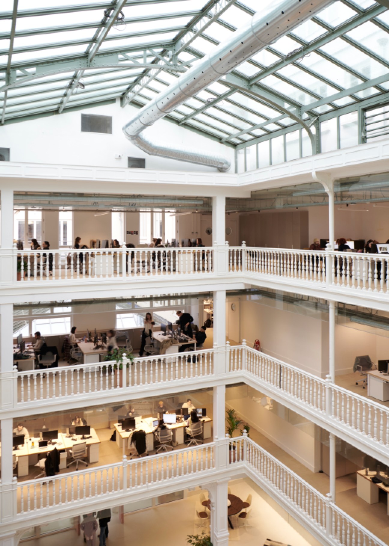 Multi-story office atrium with glass ceiling, white railings, and workers on different levels