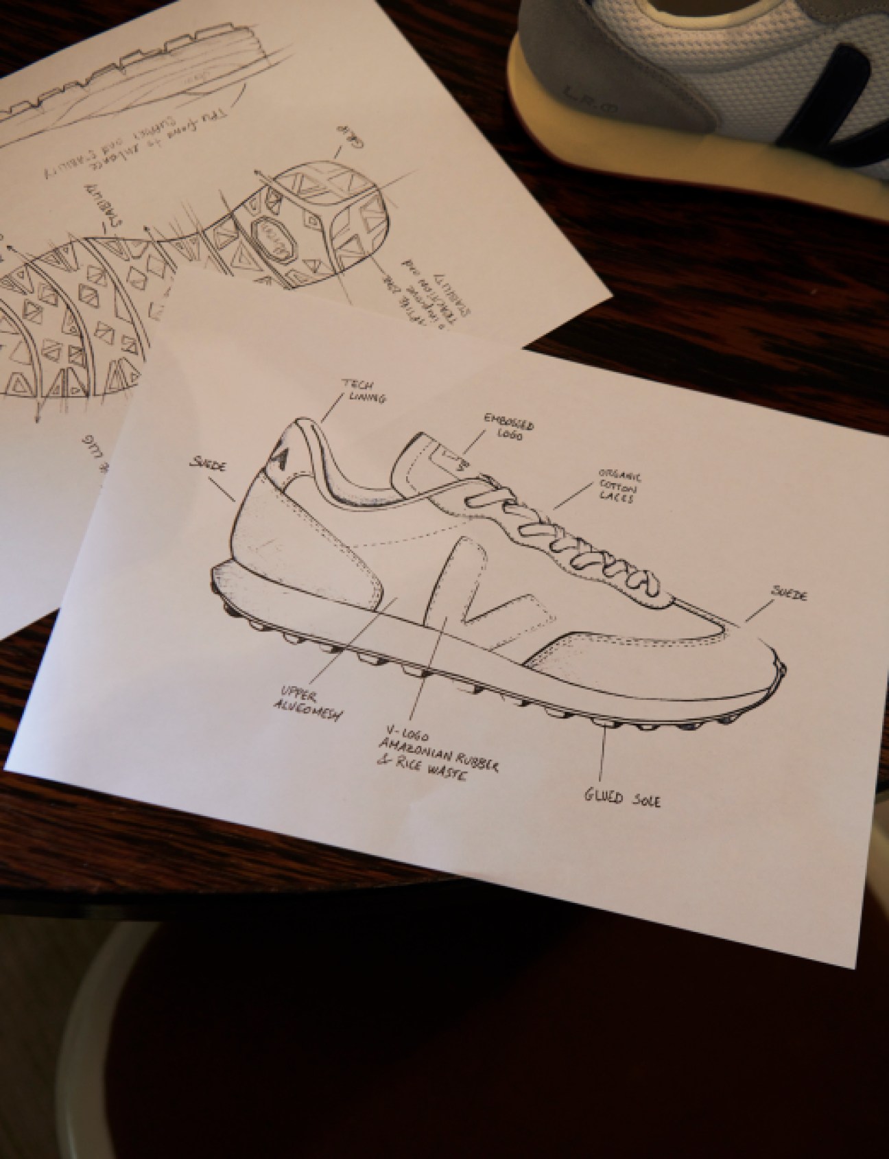 Hand-drawn sketches of sneaker designs with labeled components and materials on white paper