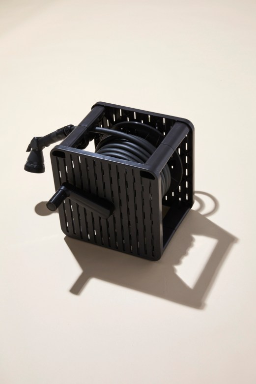 Black plastic garden hose storage crate with coiled hose and spray nozzle against neutral background