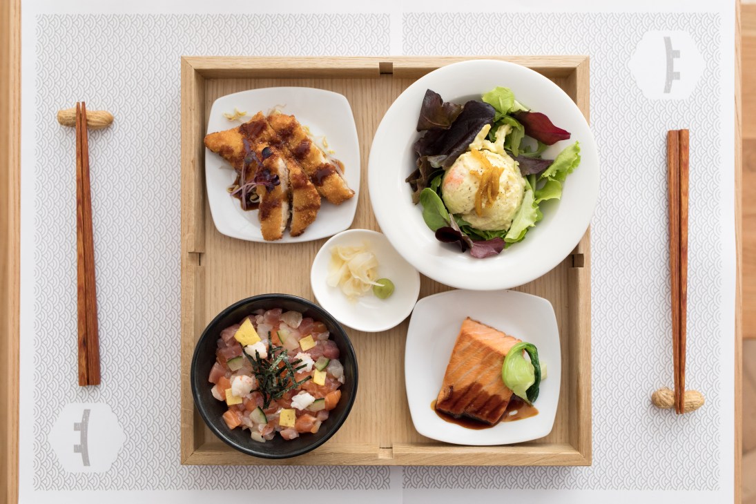 Japanese otsumami dishes arranged in a wooden tray at Tokyo Table Milan, including fried squid, salmon salad, tuna bowl, and pickled vegetables.