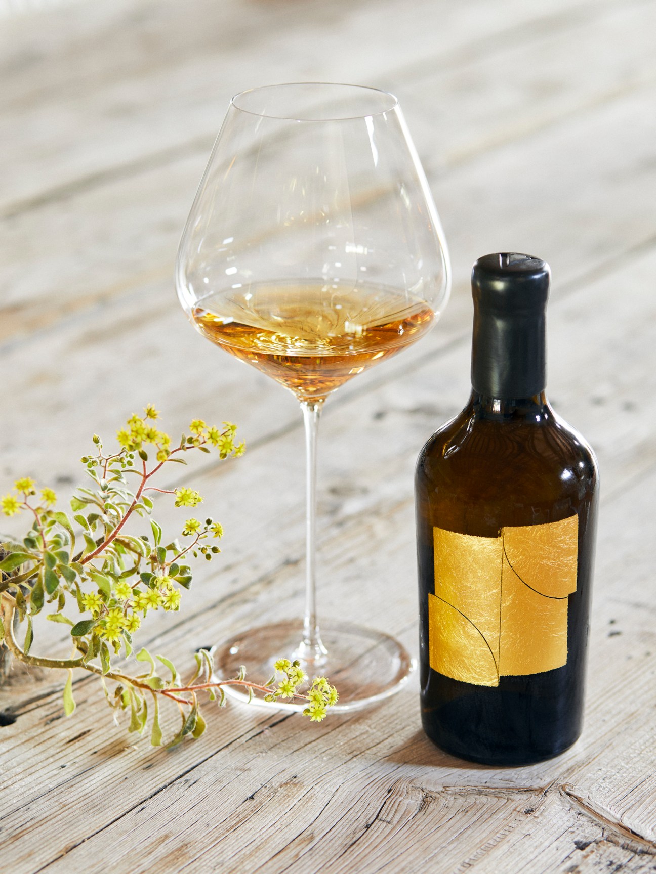Venissa's flagship wine bottle with golden label next to wine glass containing amber wine on wooden surface