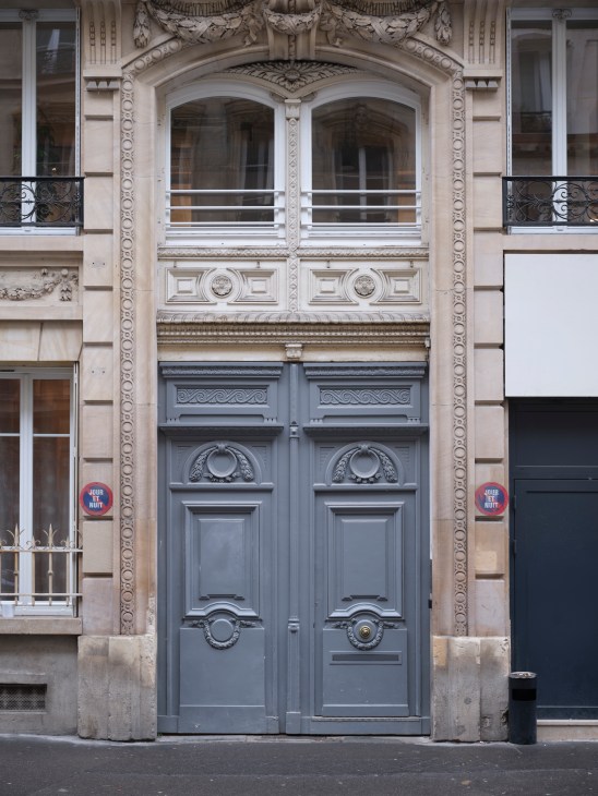 Ornate entrance to a 19th-century Parisian building with elaborate stone archway, decorative moldings, and blue double doors