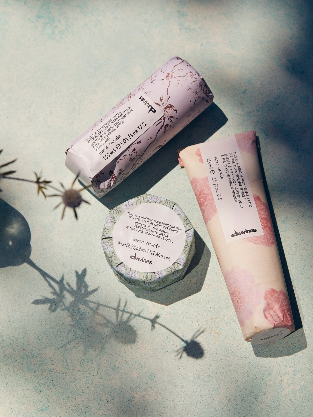 Three Davines cosmetic products with botanical packaging arranged on a textured surface with plant shadows
