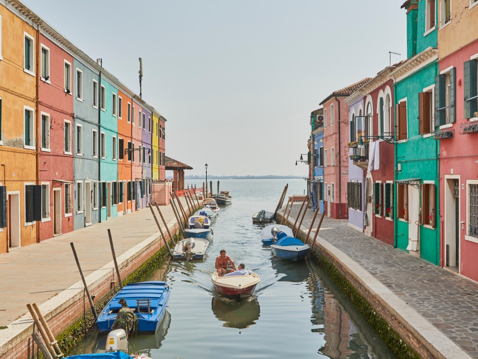 Colorful houses line a canal with boats moored along the waterway in Burano