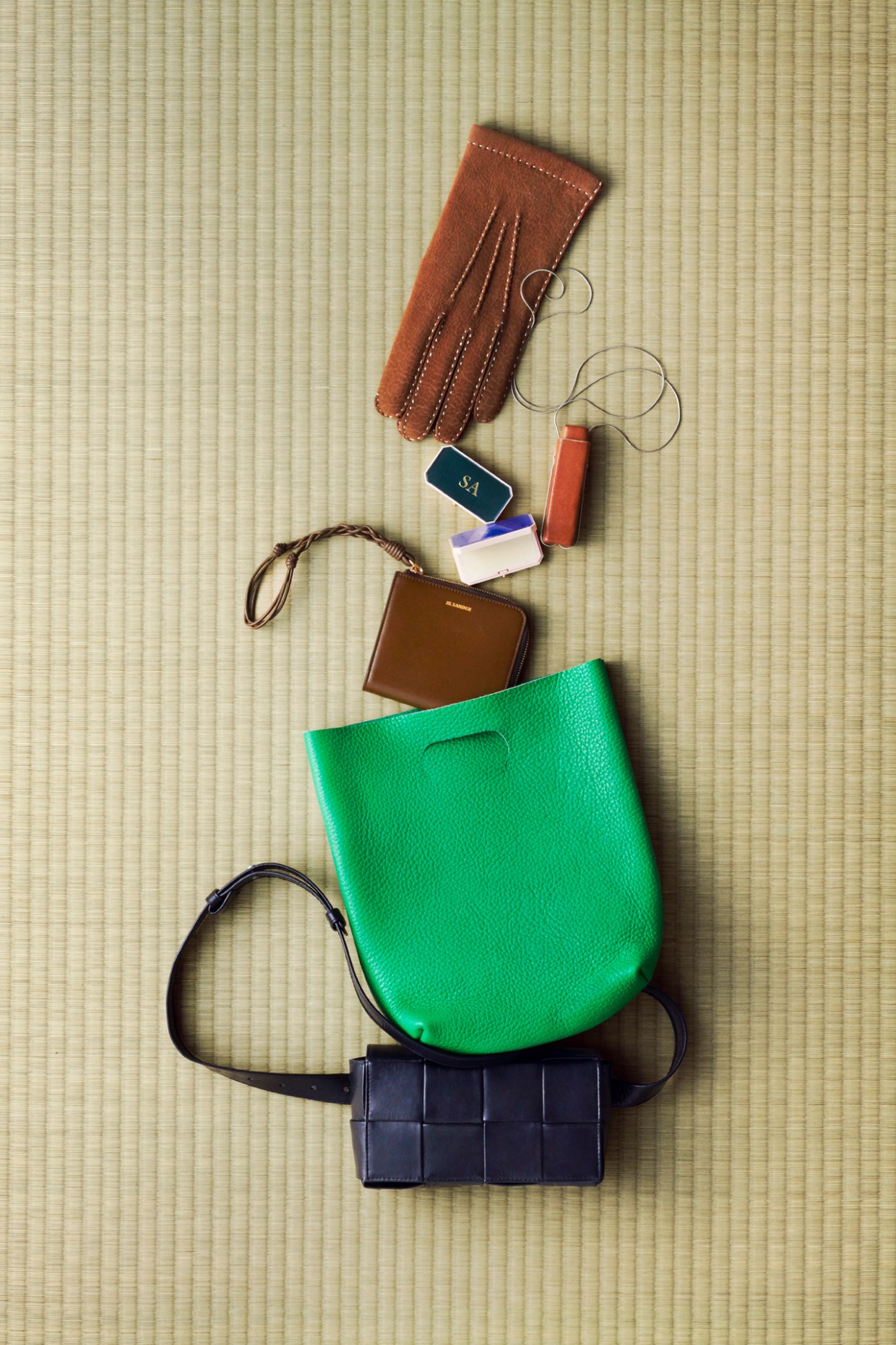 Brown leather gloves, lipstick cases, lip balm holders, credit card purse, green bag and belt bag on woven mat