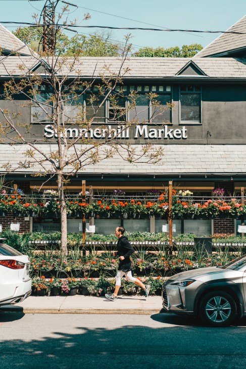 A person jogging past Summerhill Market storefront with flowering plants displayed outside